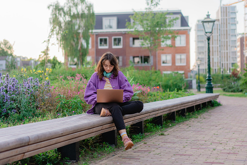 Woman sitting with laptop on the bench in the park  and working