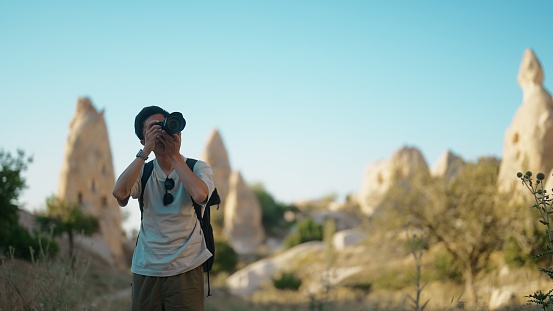 A young male photographer videographer tourist is taking photos and videos with his camerain Cappadocia.