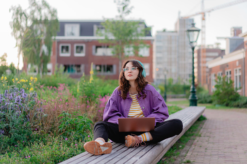 Woman sitting with laptop on the bench in the park  and working