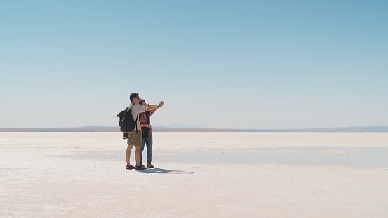 A young tourist couple is taking selfies on white salt in Salt Lake.