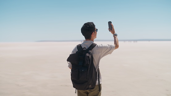 A young male tourist is taking videos and photos with his mobile phone on white salt in Salt Lake.