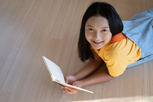 Young girl lay down on wood floor with book at home.