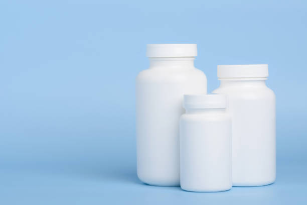 три белые пластиковые бутылки с таблетками или добавками на синем фоне - pill bottle bottle medicine white стоковые фото и изображения