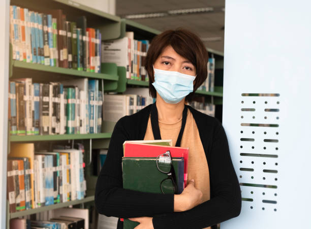 istock Woman with face mask searching data and select book for research on shelf 1413838063