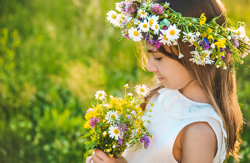 Girl lying on the grass with her two brothers looking up into the camera. Hippie style with chamonmile floral garland on her head.