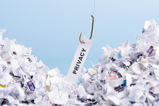 Word Privacy hooked on fishing hook pulled from pile of shredded documents on blue background