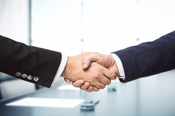 Two businessmen shake hands on the background of bright conference room, investing concept, close up stock photo