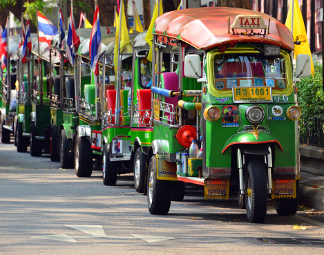 Bangkok, Thailand: downtown tuk-tuk stand - line of flag decorated 3-wheeler auto-rickshaws waiting for passangers. Tuk-tuks got their name fron the engine noise of the two-stroke engines that were common in the past -  Na Phra That Alley - Phra Nakhon district, the central district of Bangkok