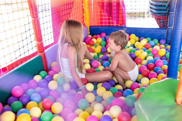 istock The older sister plays with her younger brother and throws small balls at him while sitting in the playroom 1413841233