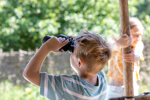 A side-view shot of a young boy having a fun time standing on a porch in the North East of England. He is using binoculars to look at the view.