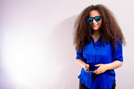 Girl with afro style hair smiling with blue glasses in copy space white background
