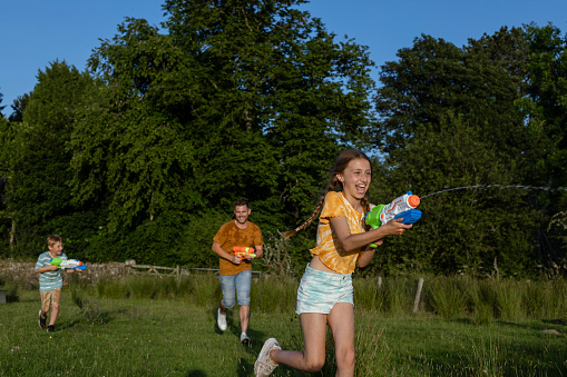 A father and his young son and daughter having a great time playing on the grass in a field in the North East of England. They are enjoying quality time together during a water gun fight.