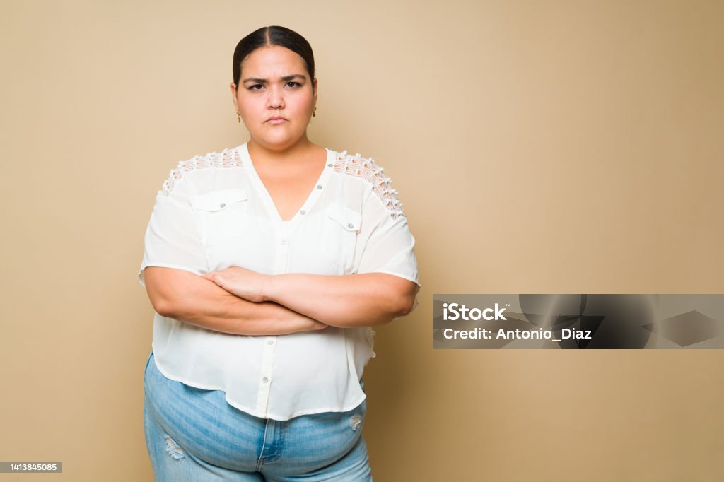 Upset fat woman looking annoyed and looking at the camera Angry hispanic young woman looking upset and annoyed after arguing or having a fight against a yellow background with copy space Anger Stock Photo