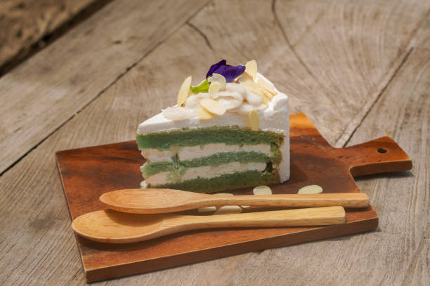 istock front view butterfly pea cake with three layer of cake on top by coconut and sprinkle with almond slices and two light brown wooden spoons, on wooden chopping board, food, sweet, dessert, copy space 1413845452