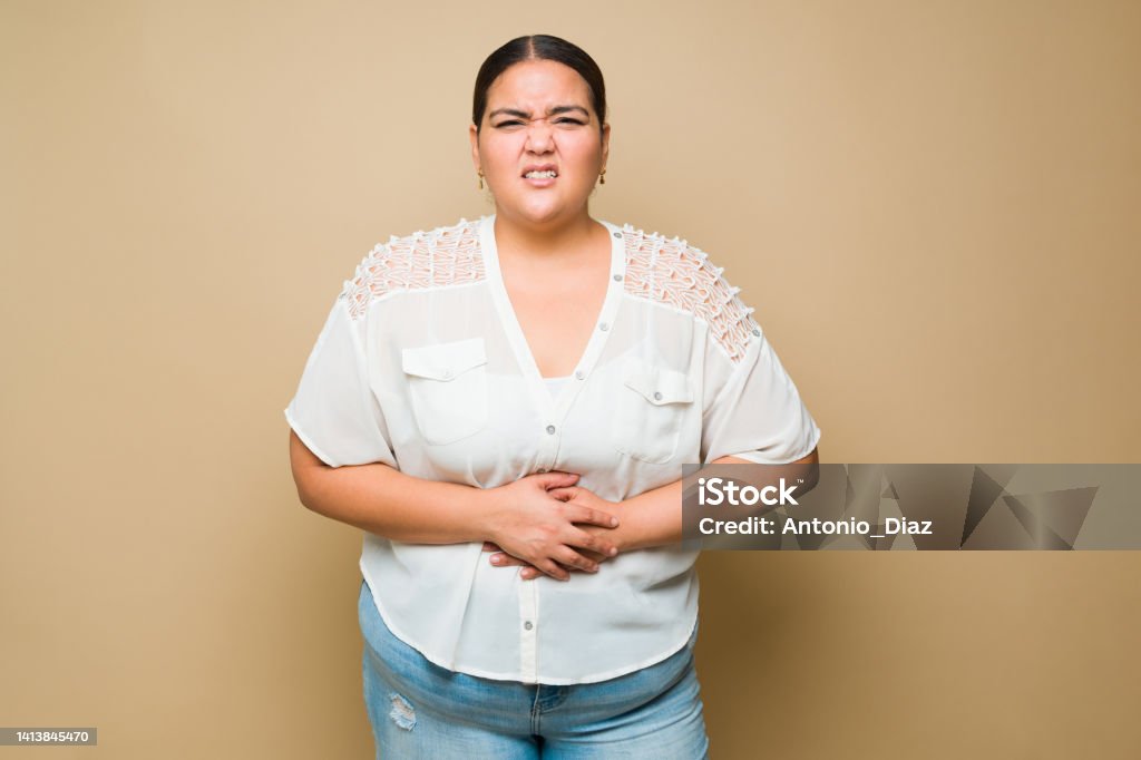 Ill fat woman suffering pain from a stomachache or indigestion Sick overweight woman touching her abdomen and feeling pain because of a stomachache or cramps Stomachache Stock Photo