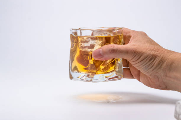 Bicchiere di whisky e cubetti di ghiaccio su sfondo bianco, uomo che tiene il vetro. - foto stock