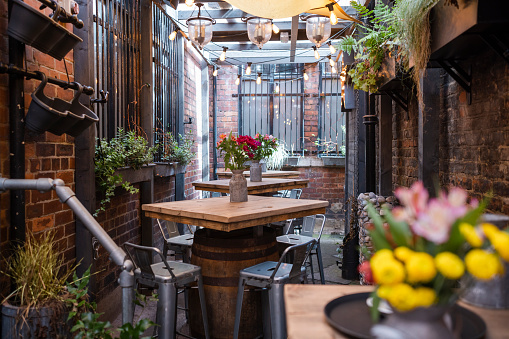 Location shot of a beer garden in the North East of England.  There are tables with flowers on them and string lights hung above.