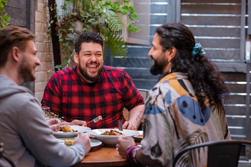 Group of mixed ethnic male friends sitting outdoors in a pub garden having a drink and meal together in the North East of England.
