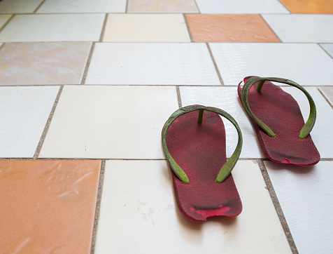 Long worn and worn shoes are placed on a ceramic tile floor.