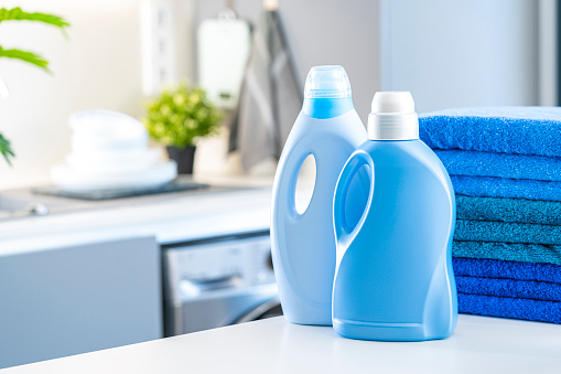 Blue fabric softener and detergent bottles shot on kitchen counter with washing machine and blue towels at background. Selective focus on bottles. Digital capture taken with Sony A7rII and Sony FE 90mm  digital capture taken with Sony A7rII and Sony FE 90mm f2.8 macro G OSS lens