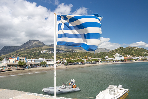 Greek Flag at Plakias in Municipality of Agios Vasileios on Crete, Greece, with boat names in the background.