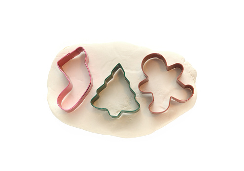 Closeup of Christmas cookie cutters on dough on a white background.