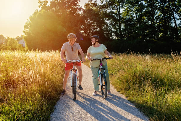 暖かい晴れた日に田舎で一緒に自転車に乗って幸せな笑顔のシニアカップル。 - senior adult action cycling senior couple ストックフォトと画像