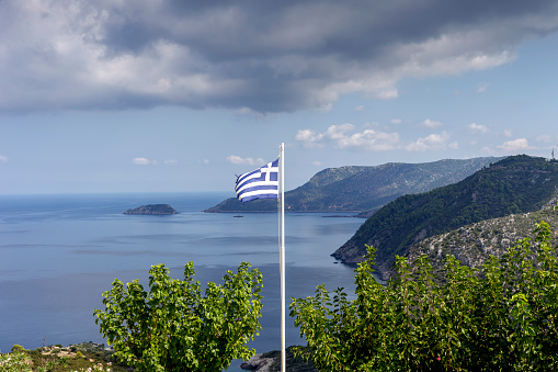 The Greek flag flies against the background of mountains, sea and sky on a sunny, summer day