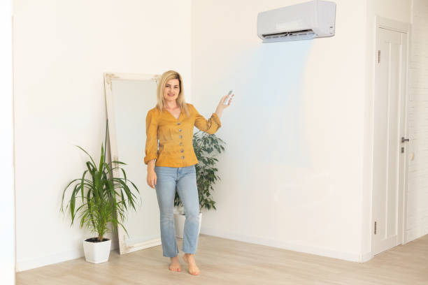 istock Woman holding remote control aimed at the air conditioner 1413855166