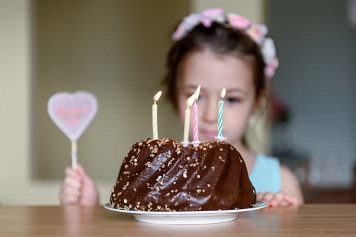 Cute little girl is sitting in front of her birthday cake and making a wish. Birthday party, celebration, chocolate cake