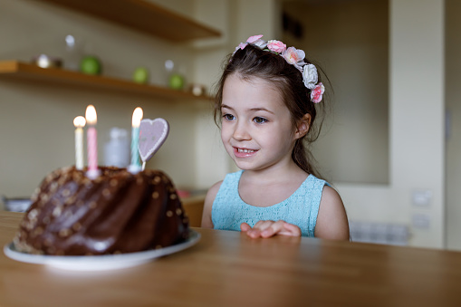 Happy and joyful adorable little girl makes a wish in front of her chocolate birthday cake
