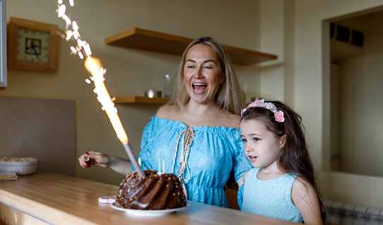 Single mother and daughter admire the fireworks on the girl's birthday cake. Birthday party at home