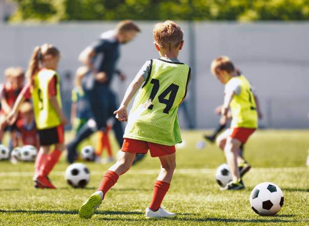 i bambini delle scuole giocano a calcio calcio con l'allenatore. bambini che calciano palloni sportivi sul campo in erba. pratica del calcio per i giovani - calcio internazionale foto e immagini stock