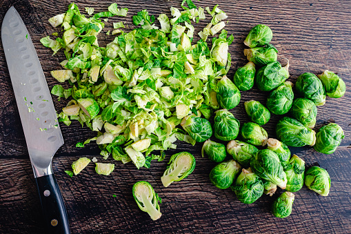 Pile of Sliced and Whole Brussels Sprouts with Chef's Knife: Halved and thinly sliced Brussels sprouts on a dark wood table