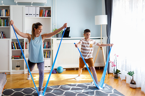 Cute boy and his mother exercising with elastic bands. Mother helping son to exercise correct.