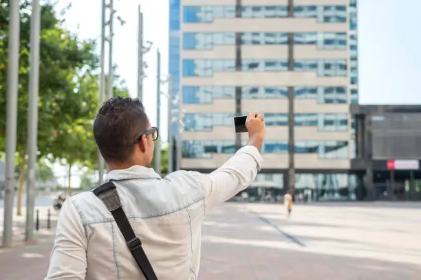 Photo of Young man wearing sunglasses taking photo in the city with a phone