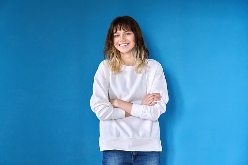 Portrait of teenage smiling female looking at camera on blue background. Positive confident successful young female student with arms crossed. Youth, beauty, success, education, confidence concept