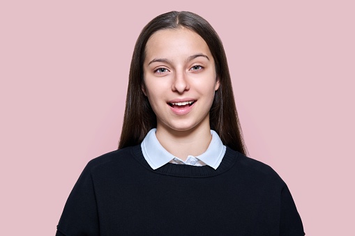 Portrait of teenage student girl cheerful looking at camera on pink color studio background. Smiling attractive positive teenager, happiness, high school, adolescence, youth concept