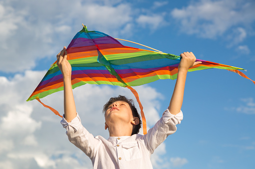 A teenage boy with a smile launches a bright kite into the sky on a summer day.