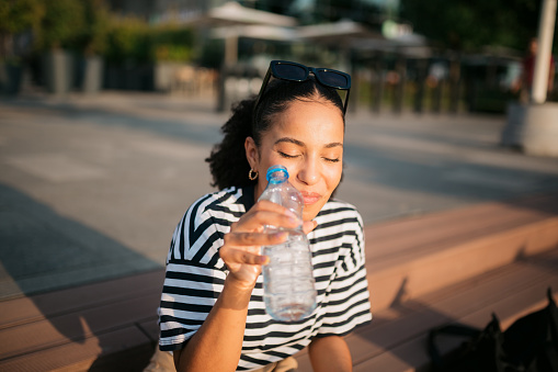 Happy young adult woman enjoying herself outdoors and drinking bottled water