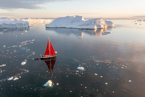 Sail boat with red sails cruising among ice bergs during dusk in front of a full moon. Disko Bay, Greenland.
Midnight sun, romantic view.
Climate change and global warming