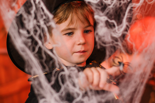 Portrait of a cute boy in a black wizard's costume in Halloween decorations.Halloween concept.Selective focus.