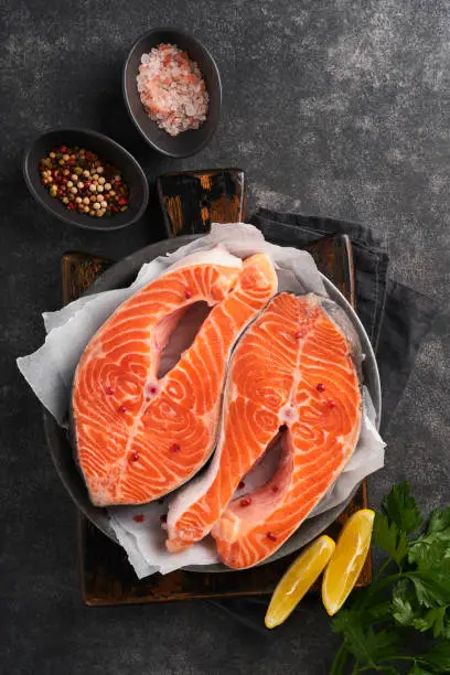 Photo of Salmon. Raw salmon steak. Fresh raw salmon fish with cooking ingredients, herbs and lemon prepared for grilled baking on black background. Healthy food. Top view. Copy space.