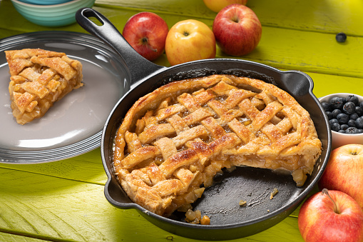 Apple pie in a cast iron skillet with apples around it.