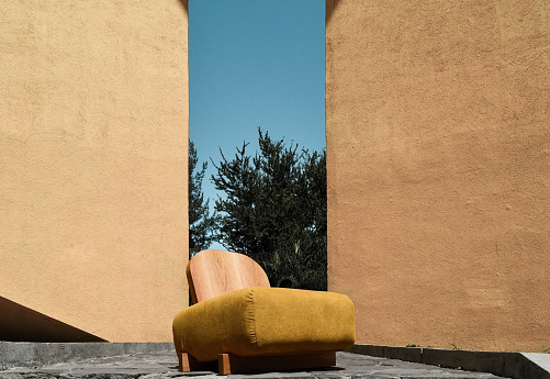 designer armchair yellow wall, wooden back and yellow textile. inside a space, with natural light in a window.