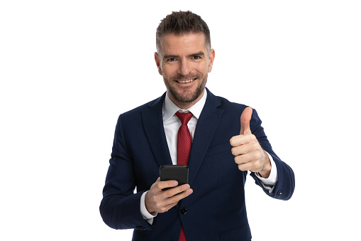 attractive businessman giving a thumbs up, holding a mobile phone and smiling at the camera