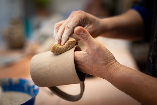Close-up of woman hands sculting and tyding up a clay cup