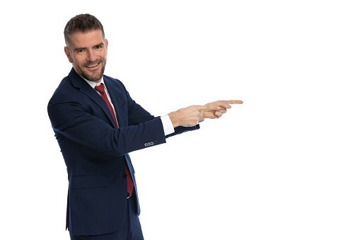 happy businessman pointing to the side and smiling at the camera against white studio background