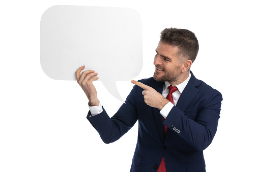 attractive businessman pointing at a speech bubble, smiling and wearing a navy suit on white background