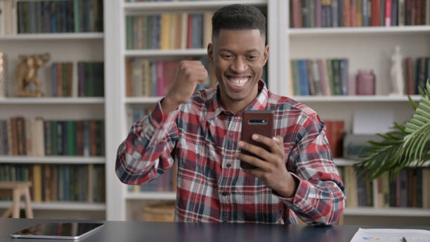 istock Successful African Man Celebrating on Smartphone 1413877575